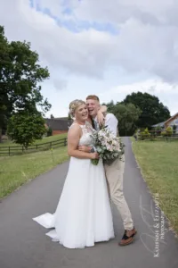 The married couple pose for their professional wedding photographs with the Blithfield Lakeside Wedding Barns behind them.